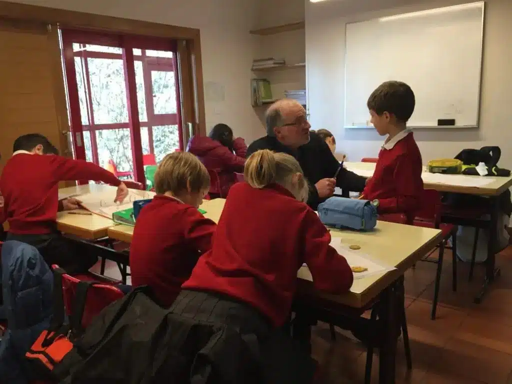 Profesor atendiendo individualmente a un alumno mientras el resto de la clase trabaja en sus mesas en el aula
