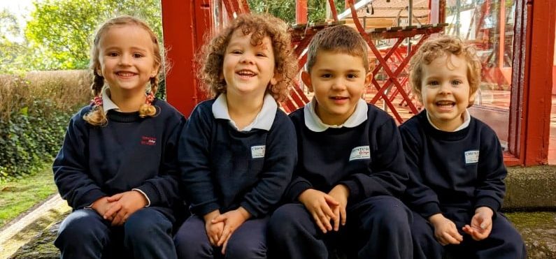 Cuatro alumnos de educación infantil sentados juntos y sonriendo a la cámara con el uniforme escolar