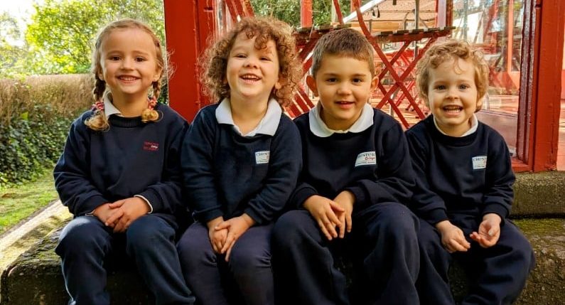 Cuatro alumnos de educación infantil sentados juntos y sonriendo a la cámara con el uniforme escolar