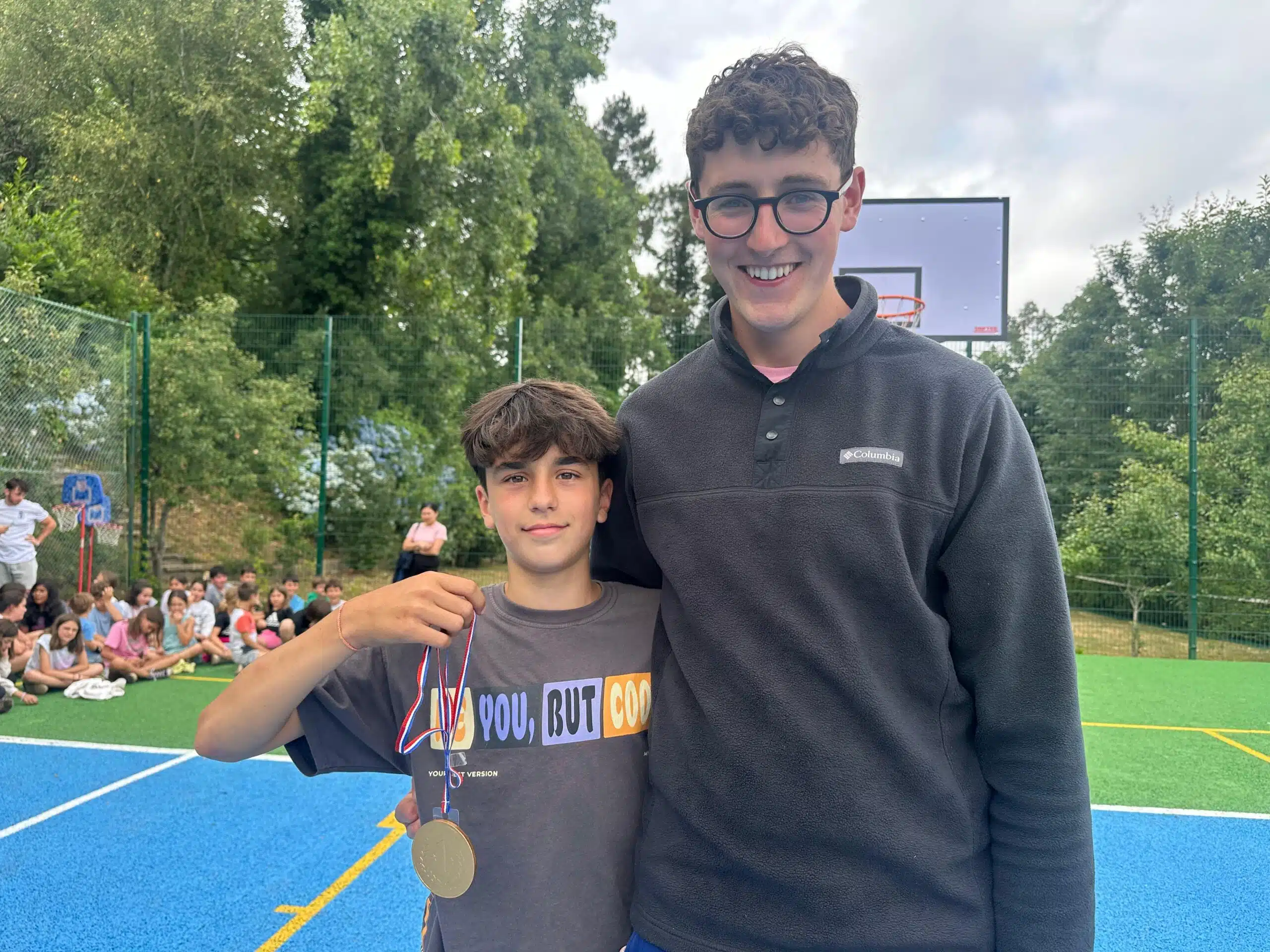 Un joven con gafas y un niño que sostiene una medalla sonríen juntos en una pista polideportiva