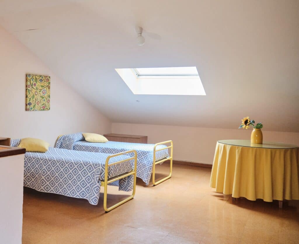 Dormitorio luminoso con dos camas individuales y techo abuhardillado en la residencia de estudiantes